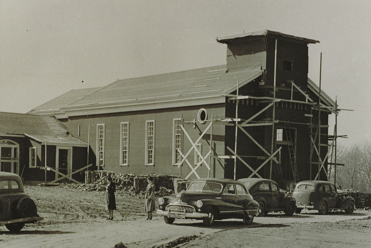 The church under construction, with scaffolding, parked cars, and two people outside.