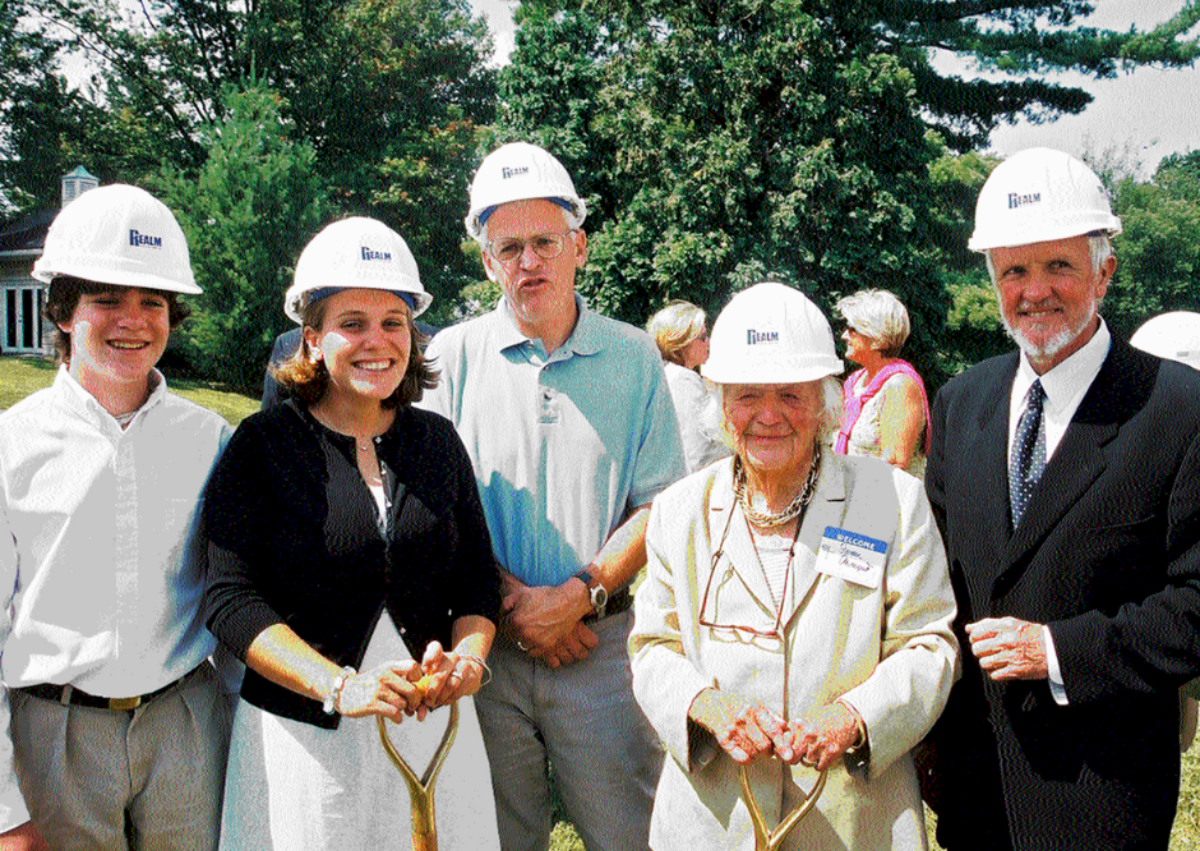 Five adults wearing hard hats pose with ceremonial shovels at a groundbreaking.