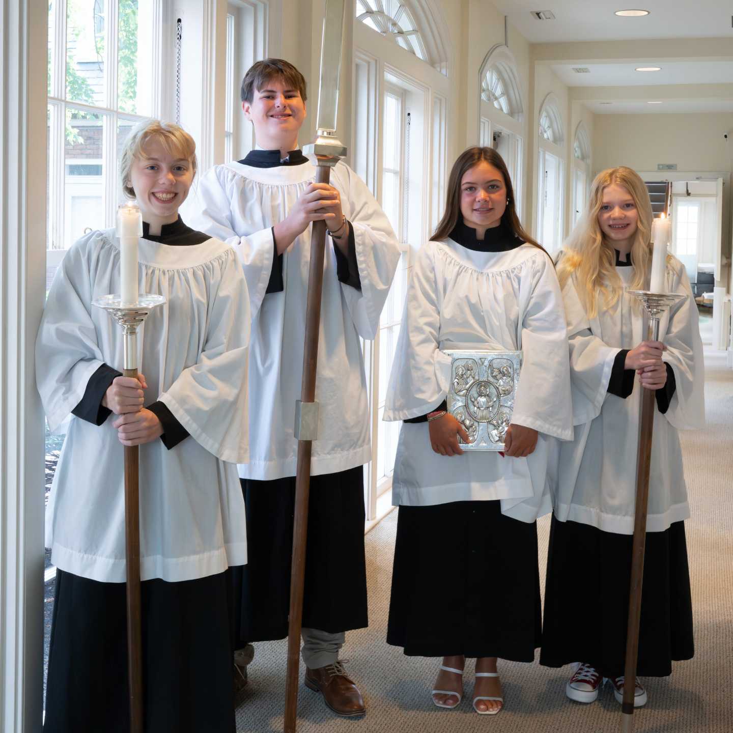 Four acolytes in white robes hold candles, a cross, and a Gospel book.