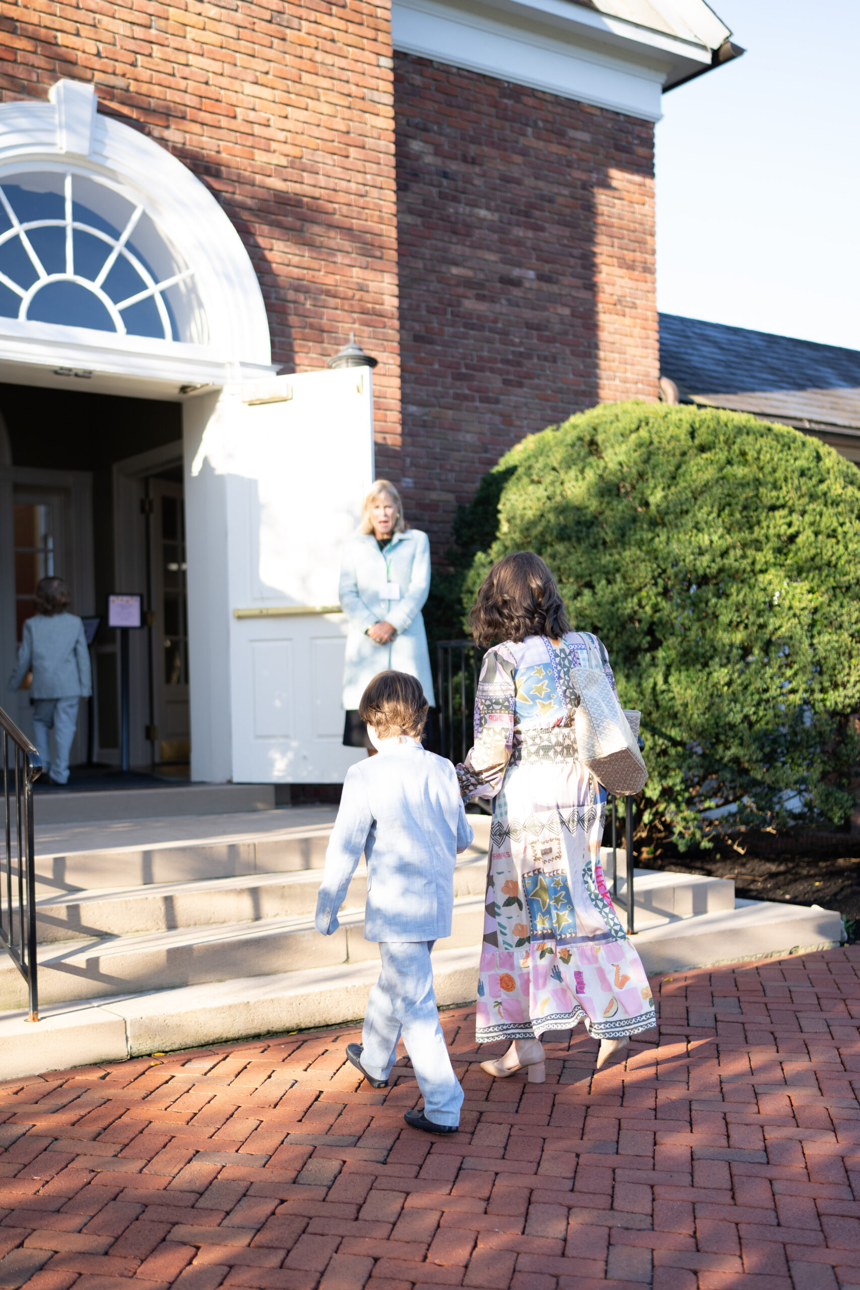 A mother and her young son approach the front door of a church, where an usher greets them.